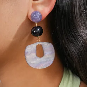 Close-up of geometric acrylic drop earrings with purple and black beads on a model.