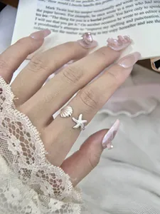 Detailed view of silver open ring featuring shell and starfish charms on finger