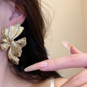 Dettaglio di un grande orecchino d'oro con texture geometrica irregolare sull'orecchio di modella