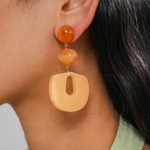Close-up of geometric acrylic earrings with marbled orange and cream segments on model's ear