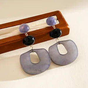 Detail view of purple and grey acrylic geometric earrings on a wooden stand.