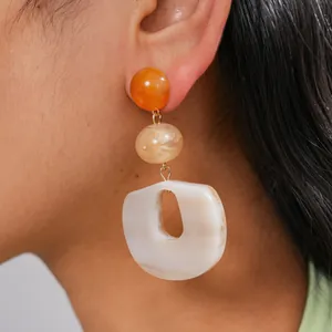 Macro detail of three-tier acrylic geometric drop earrings with marbled texture on model's ear