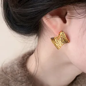 Close-up of square gold earring with textured herringbone pattern on model's ear.