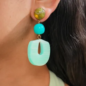 Macro detail view of a stylish acrylic geometric earring with green beads worn on an ear