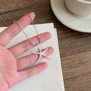 Detailed view of a hand holding a minimalist silver starfish pendant necklace on a thin chain