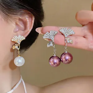 Vista detallada de elegantes pendientes de perlas y circón con hoja de ginkgo en lila