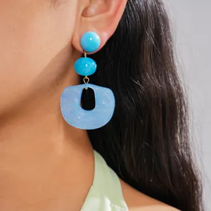 Close-up detail of marbled blue acrylic geometric drop earrings on model's ear for style
