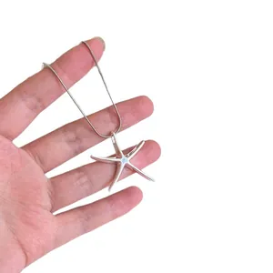 Minimalist silver starfish pendant necklace with delicate chain held by a hand in white background