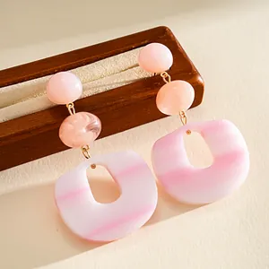 Close-up of pink acrylic geometric drop earrings with marbled beads and striped pendants.