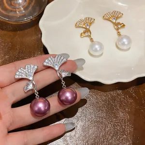 Detalle de pendientes elegantes de hoja de ginkgo con circonitas y perlas