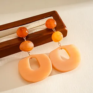 Detail view of orange acrylic geometric earrings with layered beads and oval drop.