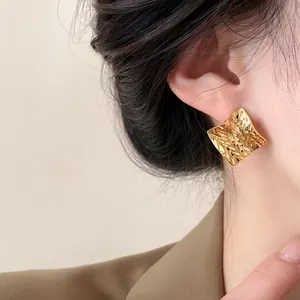Detailed macro view showing the textured pattern of a gold square stud earring worn by model