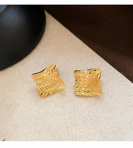 Close-up of golden square stud earrings featuring a detailed engraved geometric texture