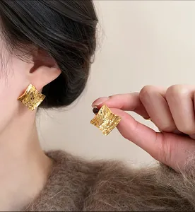 Detailed macro view of elegant square gold earrings with textured finish on model