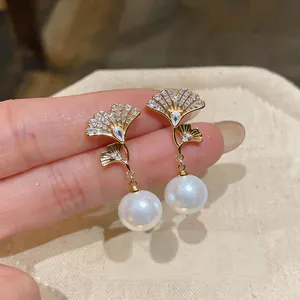 Detalle macro de elegantes pendientes de hoja de ginkgo dorada con circonitas y perlas blancas