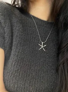 Close-up of a minimalist silver starfish pendant necklace on a gray knitted top