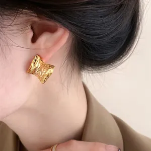 Close-up of square gold textured earring worn on ear with vintage style