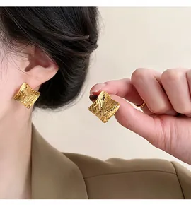 Close-up of golden square stud earrings with unique textured finish worn by a model