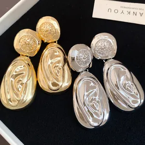 Close-up detail of textured drop earrings in gold and silver metallic finishes