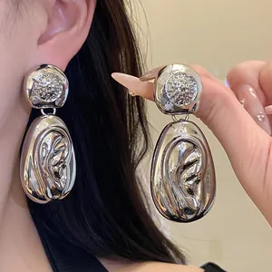 Close-up of large silver water drop earrings with unique pleated metal texture.