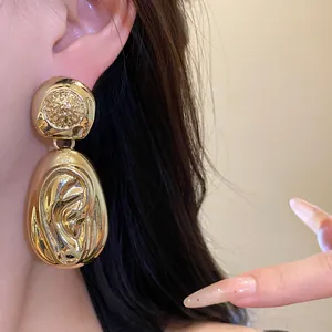 Macro detail of chunky gold drop earrings with a hammered pleated texture.