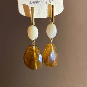 Macro detail of amber resin geometric dangle earrings with gold metal and cream beads