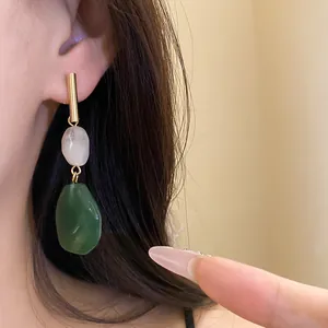 Close-up view of elegant geometric resin drop earrings featuring white and green stones