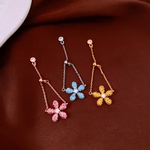 Dettaglio di anelli a fiore in zircone rosa, blu e oro con catene regolabili.