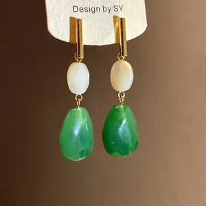 Close-up of elegant resin drop earrings with green and white stones on a display card