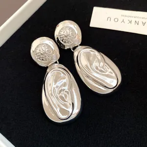 Close-up of silver-toned drop earrings with artistic wrinkled texture and metallic finish