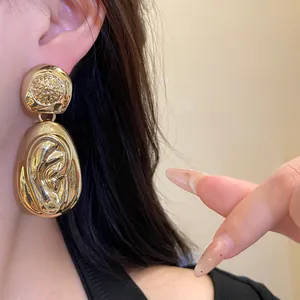 Close-up of gold chunky water drop earrings with textured ruffle design on female model