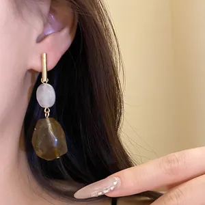 Detailed view of geometric resin drop earrings with golden bar and brown amber pendant