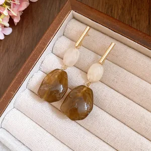 Macro view of vintage resin drop earrings with marble textures and gold bar accents