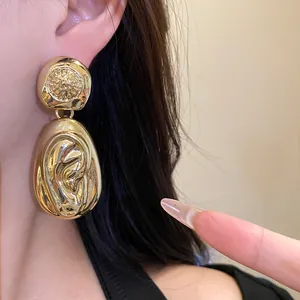 Close-up of glossy gold textured water drop pendant earrings worn on ear.