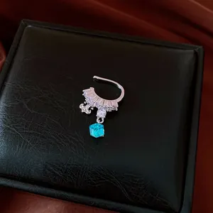 Elegant silver ear cuff with sparkling zircons and a blue crystal pendant on a black box.