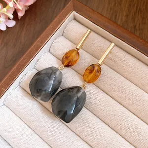 Macro detail of geometric resin drop earrings with amber and grey marble texture in a jewelry box.