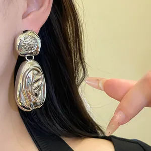 Close-up of silver-toned drop earrings featuring a bold pleated and textured metal design.
