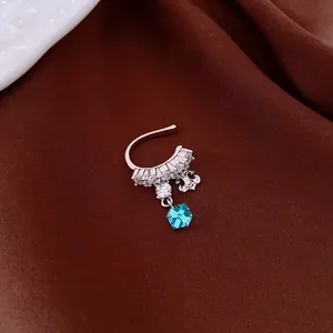 Detailed macro view of silver ear cuff with dangling blue crystal pendant on brown fabric