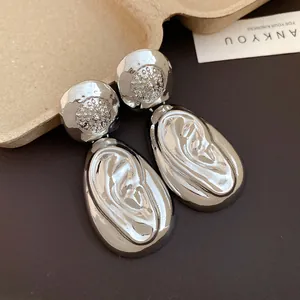 Detail view of silver drop earrings featuring a unique wrinkled texture and metallic luster.