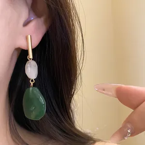 Close-up detail of gold bar drop earrings featuring white and green resin stones worn on ear