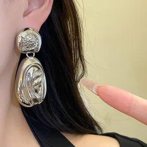 Close-up of silver-tone drop earrings with a wrinkled texture and sparkling studs