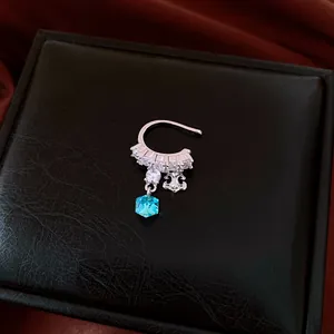 Close-up of a silver ear cuff with zircons and a vibrant blue square crystal pendant