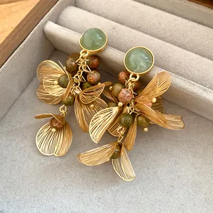 Close-up of gold filigree flower petal earrings with speckled green stone tassels in a box.