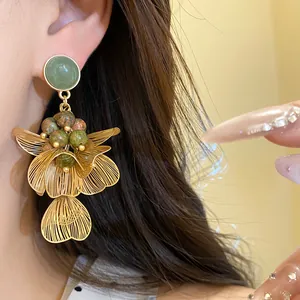 Detail of gold-tone wire petals and green stone on luxury floral tassel earrings.