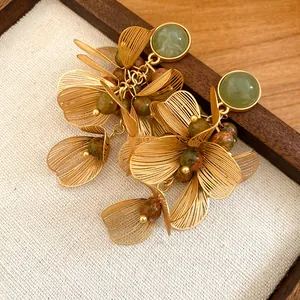Close-up of elegant gold petal earrings with colorful stone beads and green jade-like accents.
