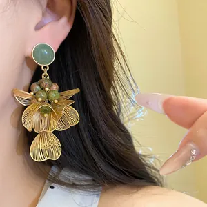 Macro detail of elegant golden wire-frame petal earrings featuring natural green stones