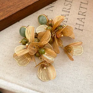 Macro detail of elegant gold-toned flower petal tassel earrings with natural green stones.