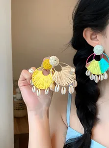 Modella asiatica che indossa orecchini in rafia a ventaglio con conchiglie kauri.