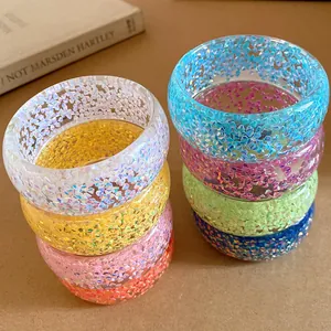 Dettaglio di bracciali rigidi in resina iridescente colorata impilati con cuori