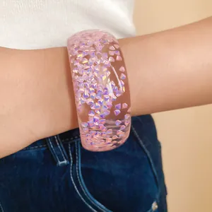 Primo piano di un bracciale rigido in resina rosa con inclusioni olografiche iridescenti.
